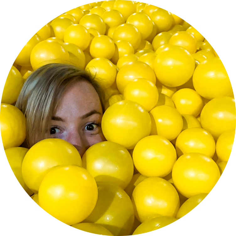 Madeline peeking out from a pit of yellow balls