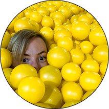Madeline peeking out from a pit of yellow balls