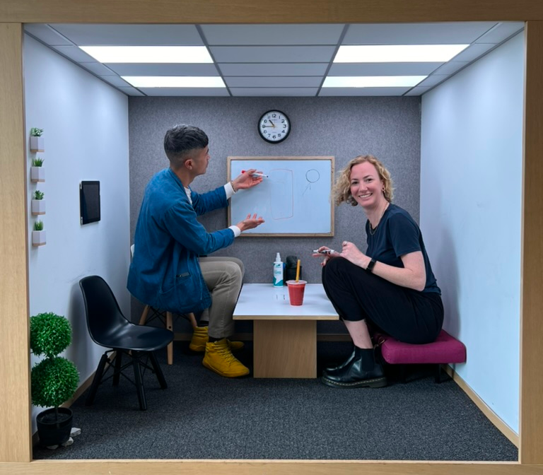 Madeline sitting with a colleague in a small office pod