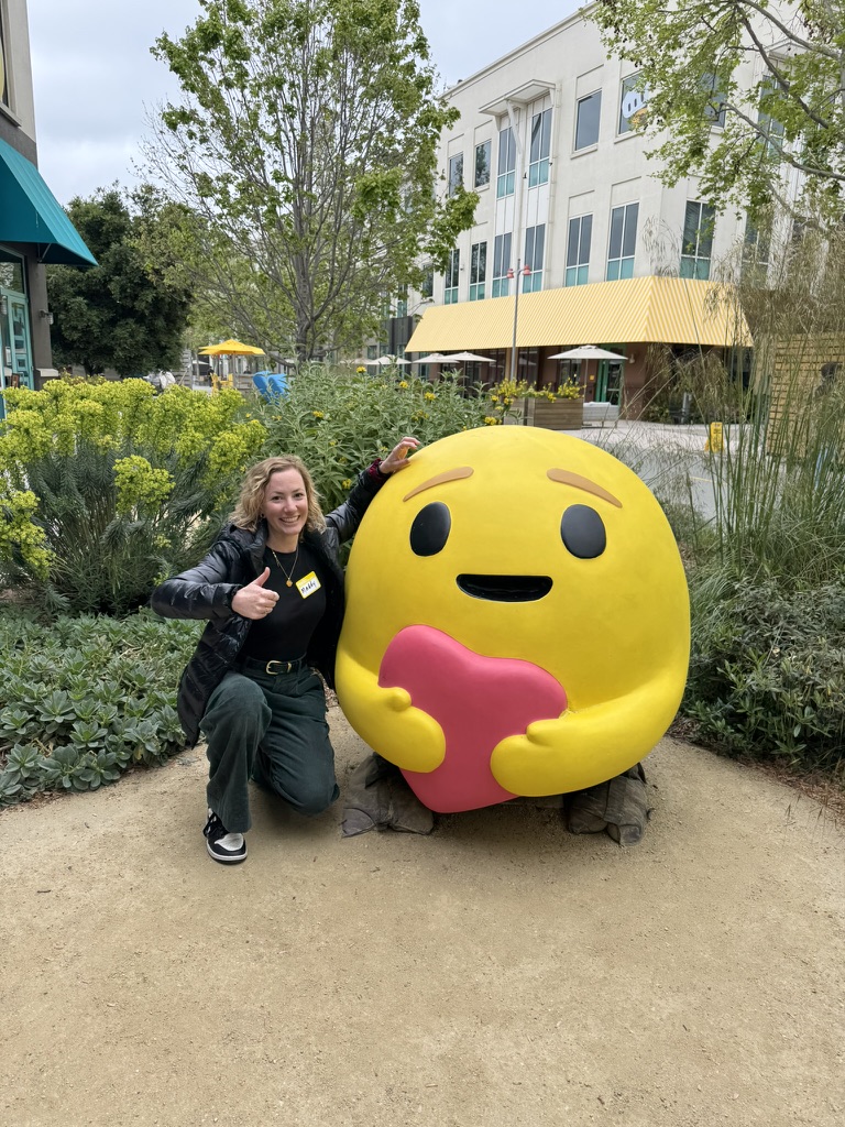 Madeline kneeling next to a large yellow heart-hugging emoji statue